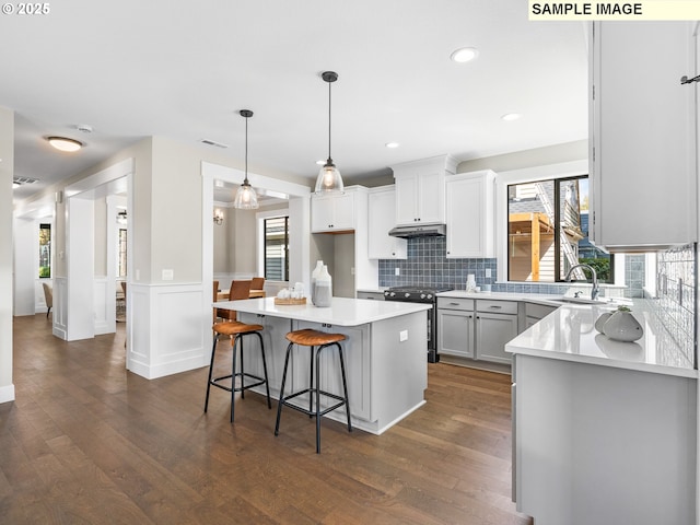 kitchen featuring a center island, stainless steel electric stove, white cabinets, sink, and decorative light fixtures