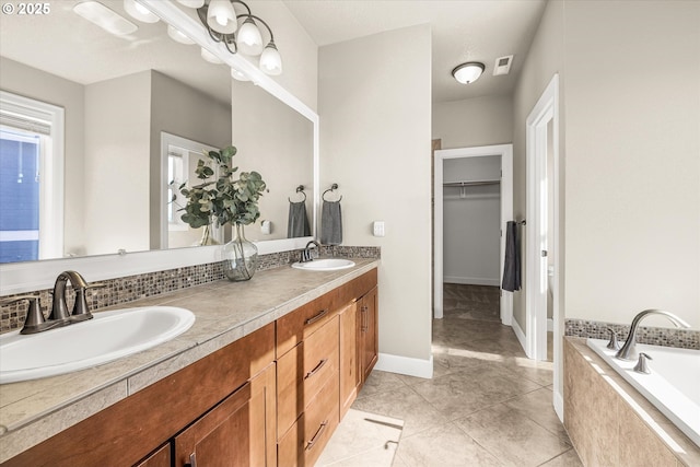bathroom with a spacious closet, double vanity, tile patterned floors, tiled bath, and baseboards