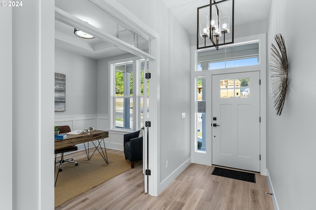 foyer featuring a wainscoted wall, light wood-style flooring, baseboards, and an inviting chandelier