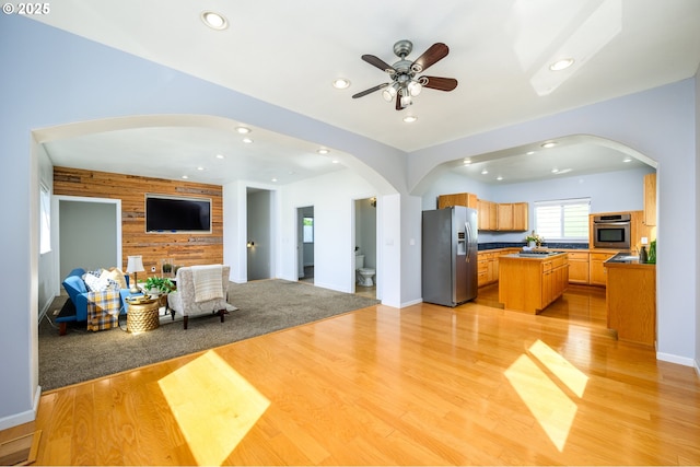 living area featuring arched walkways, wood walls, recessed lighting, and light wood-style floors