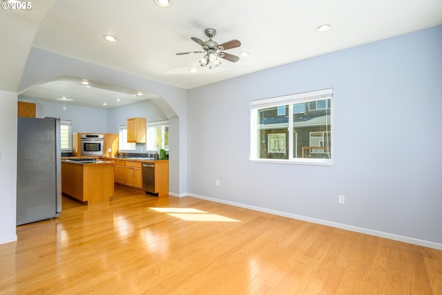 kitchen with light wood finished floors, open floor plan, stainless steel appliances, baseboards, and arched walkways