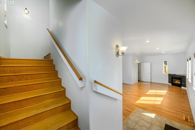 stairs featuring recessed lighting, visible vents, a glass covered fireplace, and wood finished floors