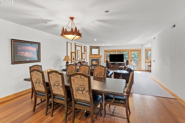 dining space with a stone fireplace, recessed lighting, baseboards, visible vents, and hardwood / wood-style flooring