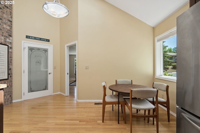 dining room featuring high vaulted ceiling, light wood-style floors, and baseboards