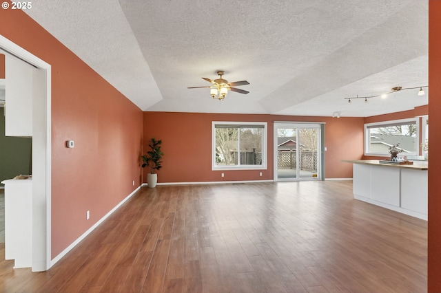 unfurnished living room featuring a ceiling fan, wood finished floors, baseboards, and a textured ceiling