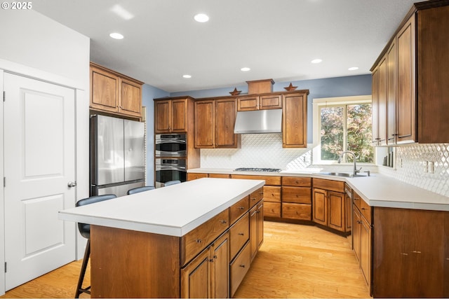 kitchen featuring under cabinet range hood, stainless steel appliances, a sink, light countertops, and a center island