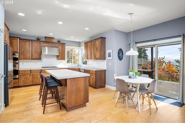 kitchen with under cabinet range hood, light countertops, a center island, brown cabinetry, and decorative light fixtures