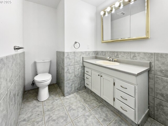 half bathroom featuring visible vents, toilet, tile walls, and wainscoting