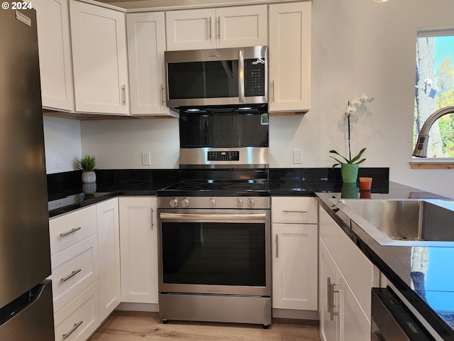 kitchen featuring white cabinets, a sink, light wood-type flooring, appliances with stainless steel finishes, and dark countertops