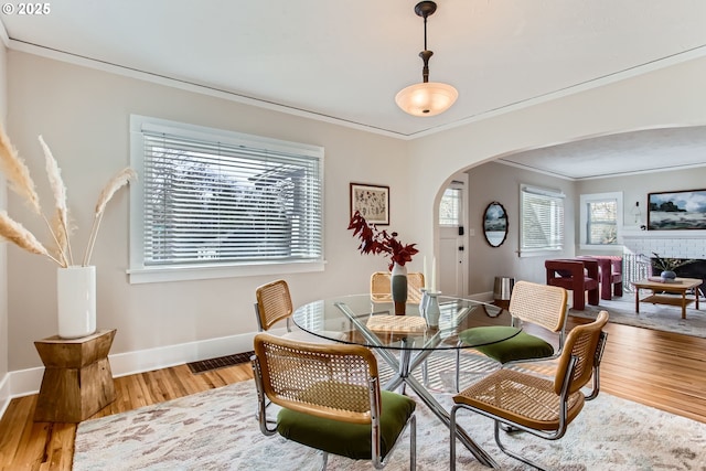 dining space featuring light wood-type flooring, arched walkways, baseboards, and crown molding