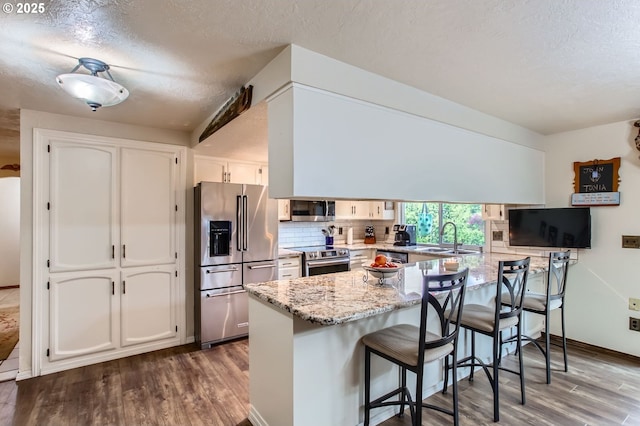 1473 N Locust St, Canby, OR 97013 - kitchen with stainless steel appliances, a peninsula, dark wood-style floors, white cabinetry, and a textured ceiling
