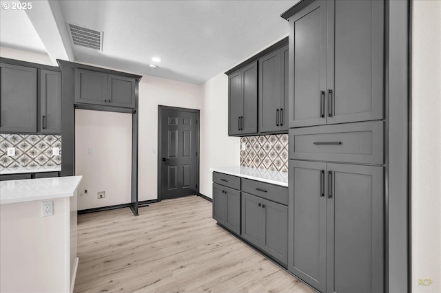 kitchen featuring visible vents, light wood-style flooring, tasteful backsplash, light countertops, and baseboards