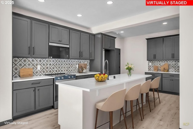 kitchen with a center island with sink, a breakfast bar area, light countertops, stainless steel range with electric stovetop, and light wood-style floors