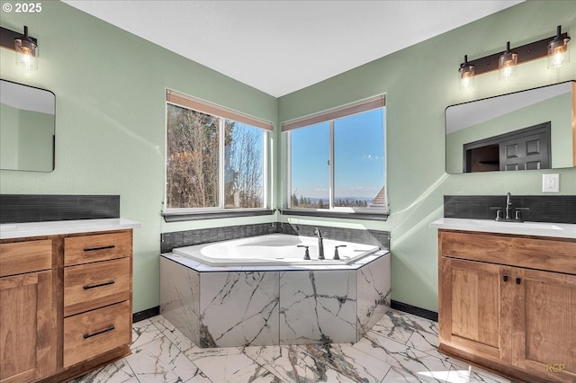 full bath featuring baseboards, two vanities, a sink, a bath, and marble finish floor