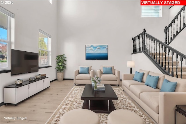 living room featuring a healthy amount of sunlight, stairs, a high ceiling, and light wood-style floors