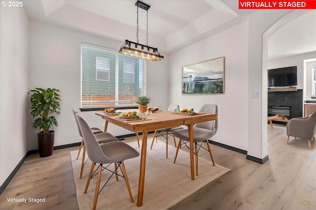 dining room with light wood-style flooring, arched walkways, baseboards, and a tile fireplace