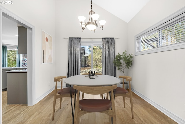 dining space with light wood-type flooring, vaulted ceiling, and an inviting chandelier