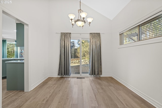 unfurnished dining area featuring lofted ceiling, an inviting chandelier, and light hardwood / wood-style flooring