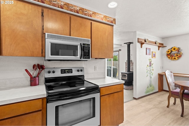 4775 Sienna Dr NE, Salem, OR 97301 - kitchen with stainless steel appliances, light countertops, a wood stove, brown cabinets, and a textured ceiling