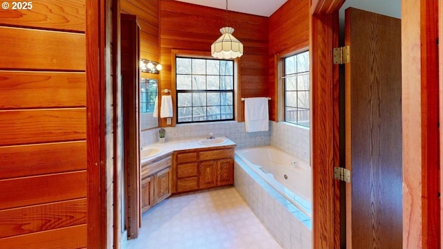 bathroom featuring tiled tub, vanity, and wood walls