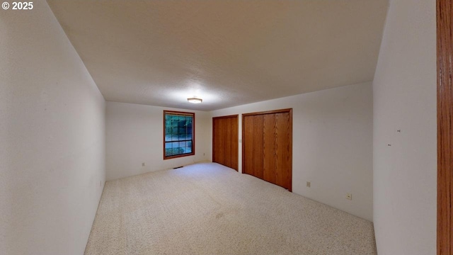 unfurnished bedroom featuring light carpet and multiple closets