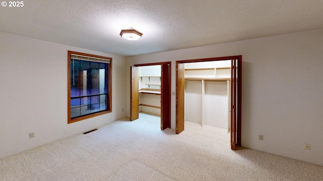 unfurnished bedroom with light carpet, two closets, and a textured ceiling