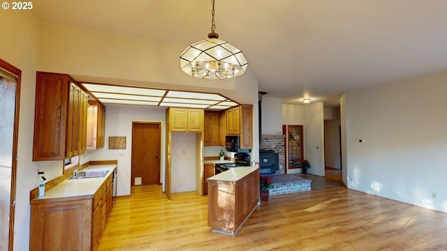 kitchen featuring sink, a wood stove, hanging light fixtures, black appliances, and light wood-type flooring