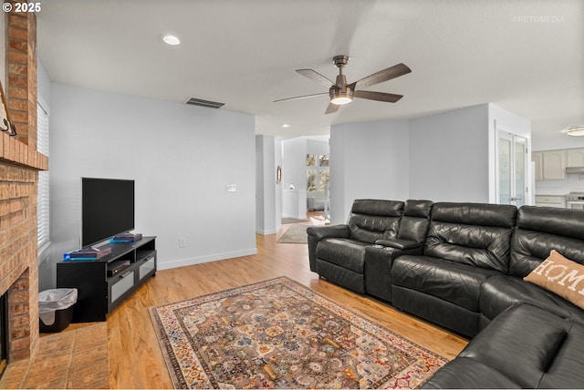 living area featuring visible vents, a brick fireplace, ceiling fan, light wood-type flooring, and baseboards