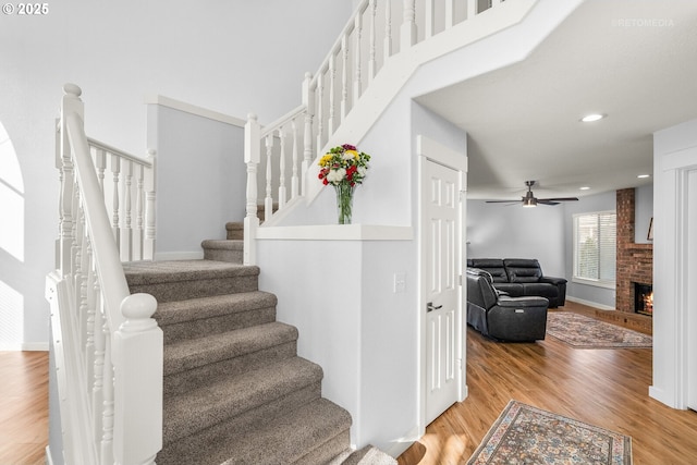 staircase featuring ceiling fan, recessed lighting, a fireplace, wood finished floors, and baseboards