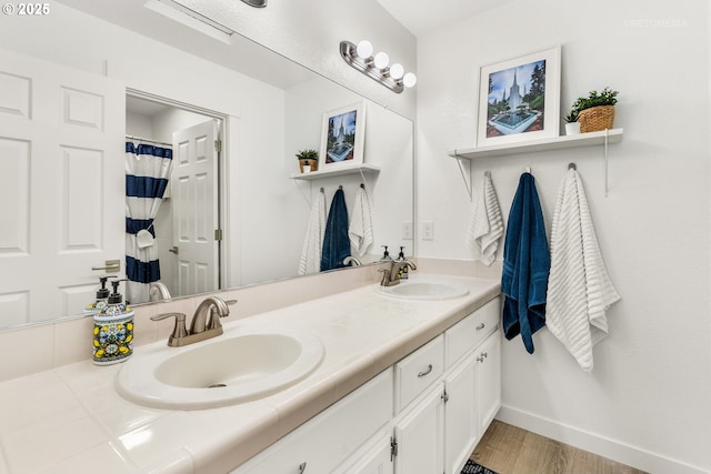 bathroom featuring double vanity, baseboards, a sink, and wood finished floors