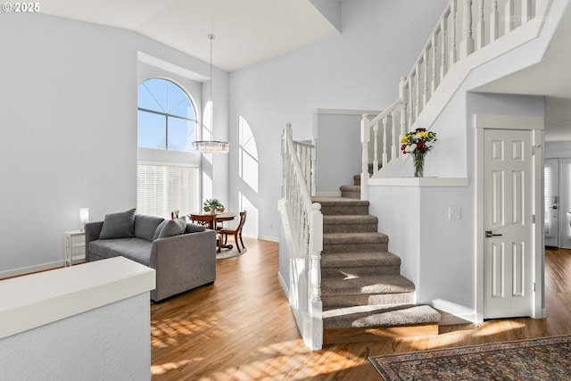 stairway with baseboards, high vaulted ceiling, a chandelier, and wood finished floors