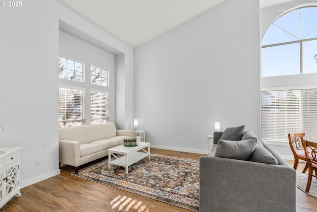 living area featuring high vaulted ceiling, baseboards, and wood finished floors