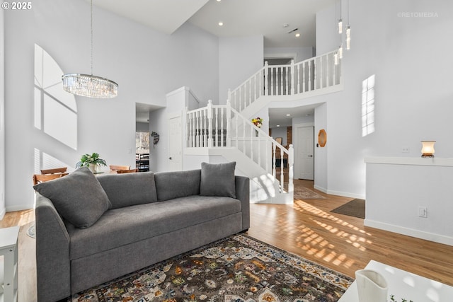 living area featuring a high ceiling, an inviting chandelier, wood finished floors, baseboards, and stairs