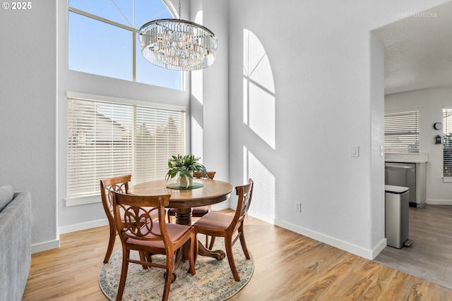 dining room with a towering ceiling, an inviting chandelier, baseboards, and wood finished floors