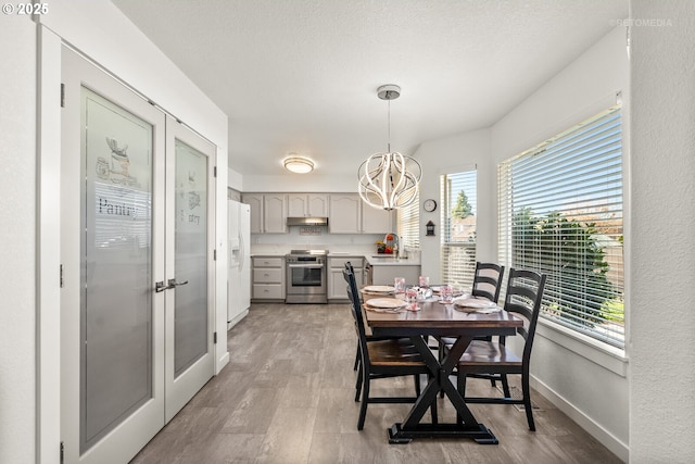 dining area with baseboards, a textured ceiling, a chandelier, and light wood-style floors