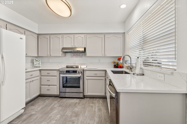 kitchen featuring light stone counters, stainless steel appliances, a sink, light wood-type flooring, and under cabinet range hood