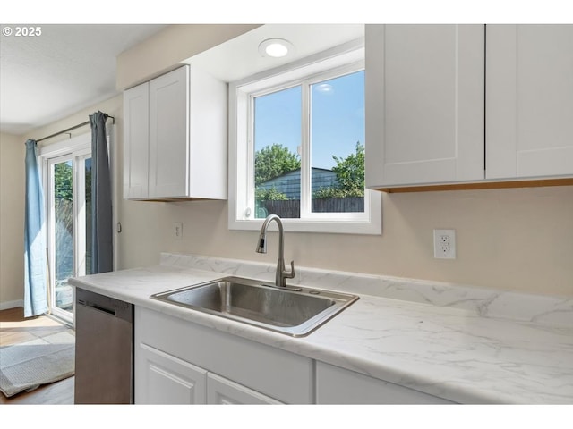 kitchen with a sink, light stone counters, white cabinets, and stainless steel dishwasher