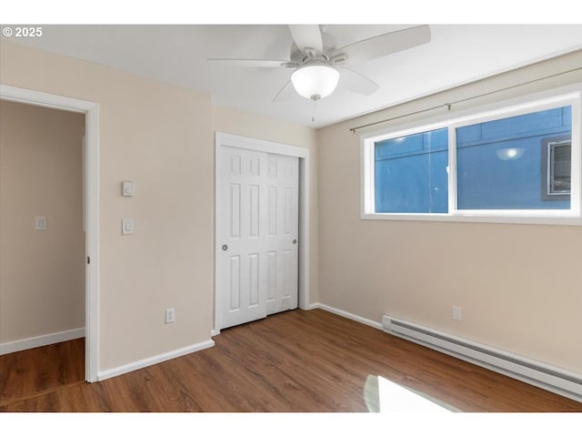 unfurnished bedroom with ceiling fan, baseboards, wood finished floors, a baseboard radiator, and a closet