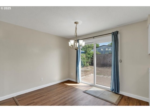 unfurnished dining area featuring baseboards, wood finished floors, and a chandelier