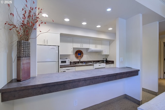 kitchen with white appliances, a sink, dark countertops, under cabinet range hood, and recessed lighting