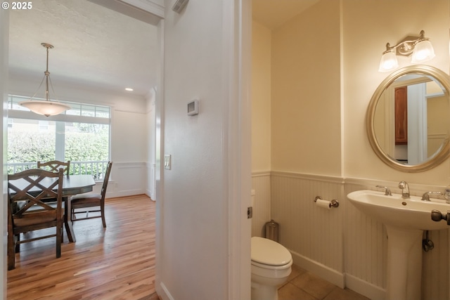bathroom featuring a decorative wall, toilet, a wainscoted wall, baseboards, and wood finished floors
