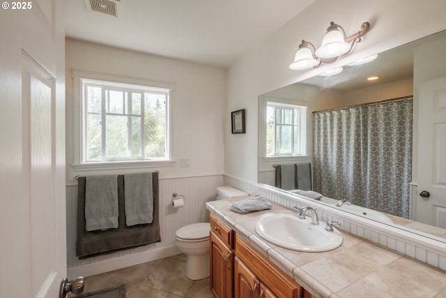 bathroom with a wainscoted wall, a wealth of natural light, toilet, and visible vents