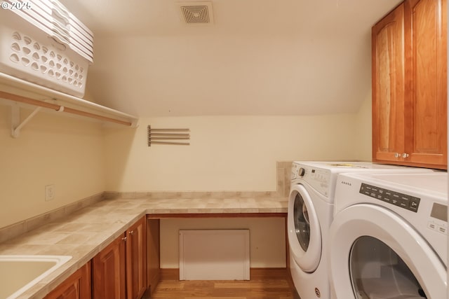 laundry room featuring visible vents, washing machine and dryer, light wood-style floors, a sink, and cabinet space