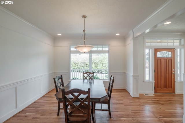 dining area featuring crown molding, wainscoting, a decorative wall, and light wood finished floors