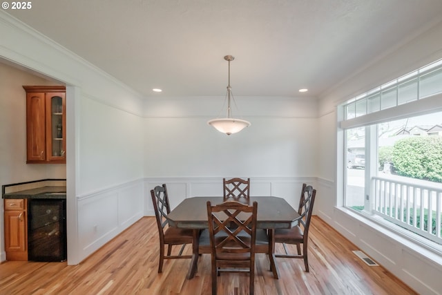 dining room featuring beverage cooler, visible vents, ornamental molding, and light wood-type flooring