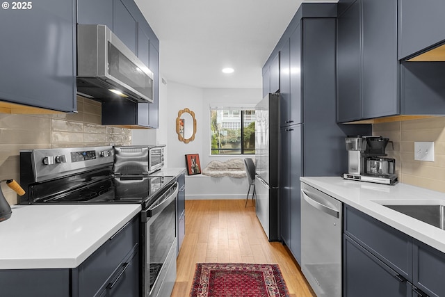 kitchen with a toaster, stainless steel appliances, light countertops, backsplash, and light wood-type flooring
