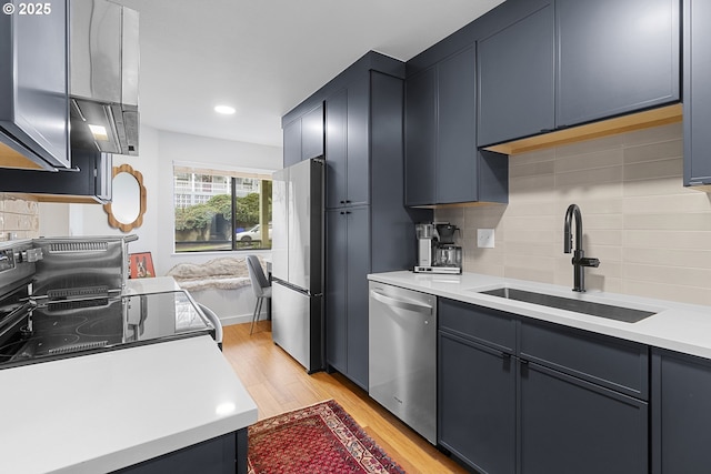 kitchen featuring stainless steel appliances, a sink, light wood-style floors, decorative backsplash, and light countertops