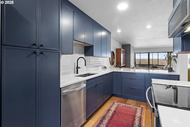 kitchen with a sink, light wood-type flooring, stainless steel appliances, blue cabinetry, and backsplash