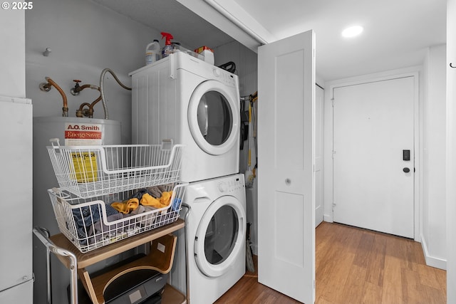 clothes washing area featuring wood finished floors, stacked washer / dryer, and laundry area