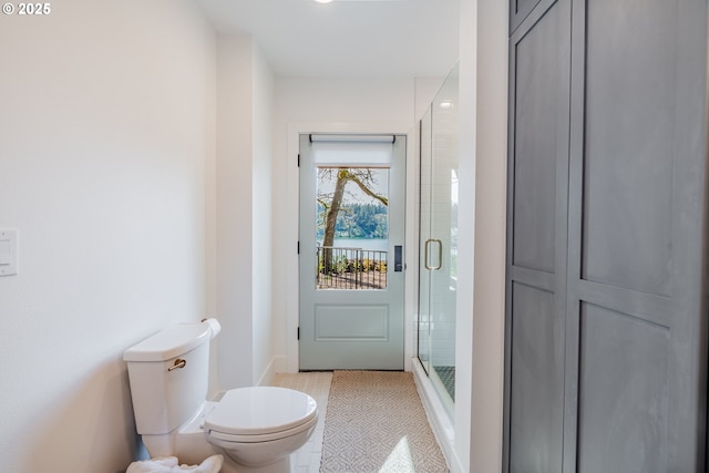 bathroom featuring toilet, a shower stall, and baseboards
